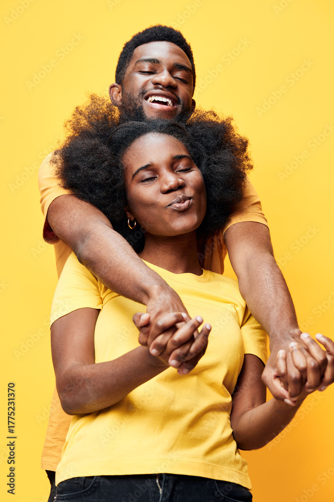 Obraz premium Joyful couple with Afro hairstyles wearing matching yellow shirts against a bright yellow background, showcasing love and happiness