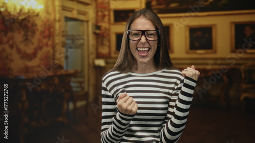 Wallpaper Mural Woman smiling with clenched fists and glasses in museum gallery, striped shirt visible; joy celebration victory. Torontodigital.ca