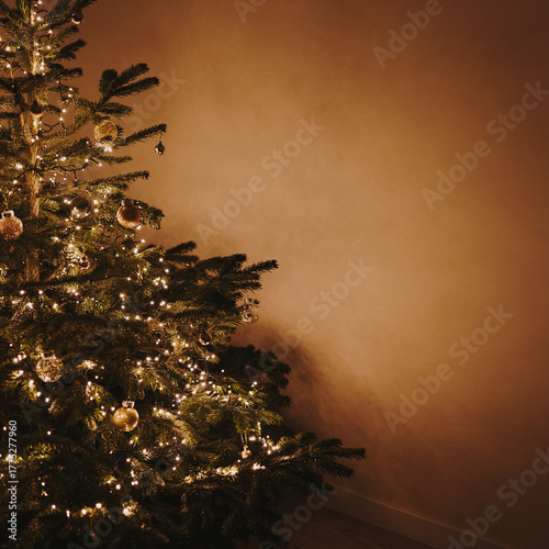 Christmas tree decorated with toys and warm garland lights on tan brown wall. Aesthetic Christmas, New Year, winter holidays composition