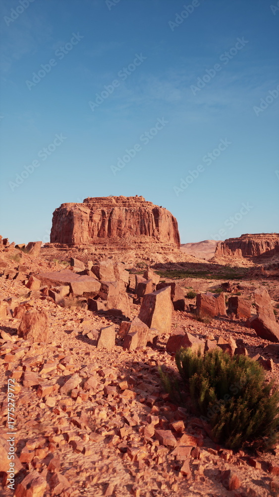 Fototapeta premium A stunning desert scene unfolds with unique rock structures and textured ground, surrounded by sparse vegetation. Under the bright blue sky, this space evokes serenity and raw beauty.