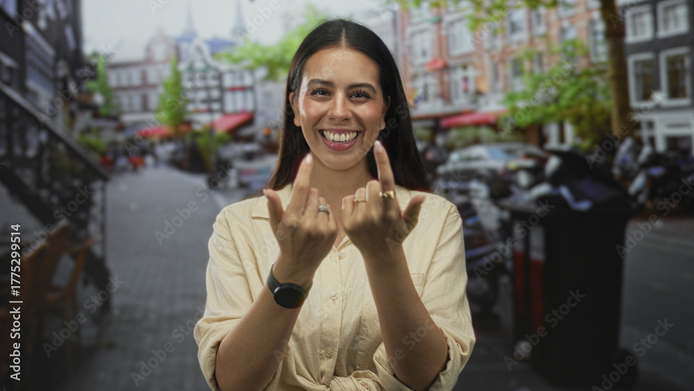Fototapeta premium Woman smiling and beckoning with fingers on a cobblestone street in the city, wearing tied shirt and rings; joy connection.