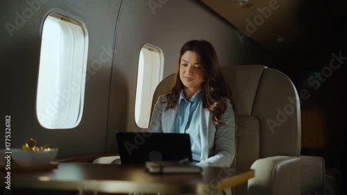 Confident businesswoman flying on a private jet and working on her laptop computer. A wealthy female entrepreneur sitting in a luxury first-class airplane cabin during a business trip
