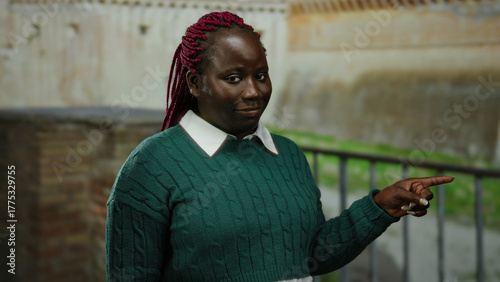 Photos Woman with braids in green sweater pointing and smiling in roman ruins outdoor background in rome city street setting displaying ancient history and culture