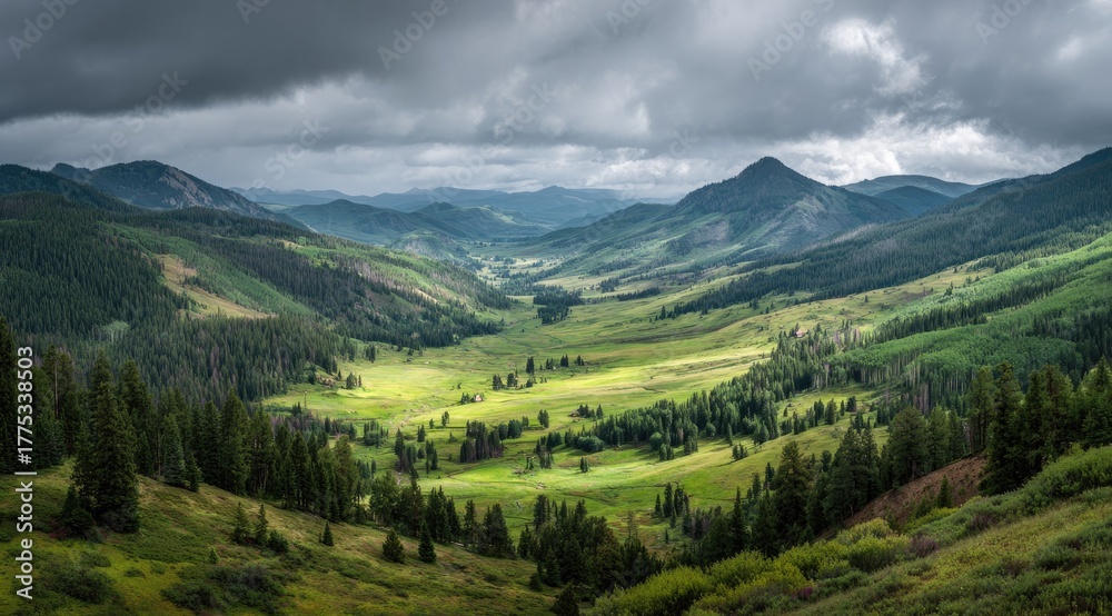 Fototapeta premium Mountain valley panorama under a stormy sky. Lush green meadows and forests nestled between rugged peaks