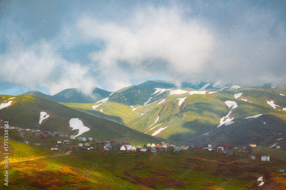 Naklejka premium Aerial view of Gomis Mta in Georgia, a mountain village with small wooden houses surrounded by snow and green hills. Peaceful and scenic highland landscape