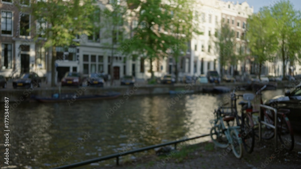 Obraz premium Blurred bicycles on amsterdam canal with classic architecture in background creating a defocused urban landscape scene bathed in soft bokeh light.