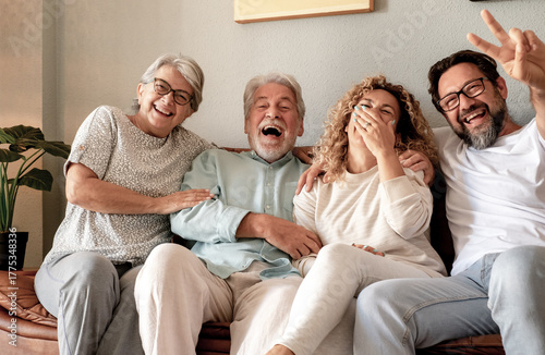 Happy multi generation family group relaxing on sofa at home having fun and laughing. Handsome people, parents and adult sons, two generations looking at camera