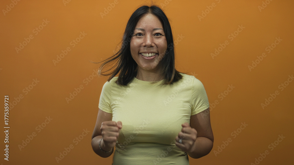 Obraz premium Young hispanic woman with clenched fists and visible hands in studio with orange backdrop, smiling and animated; joy triumph.