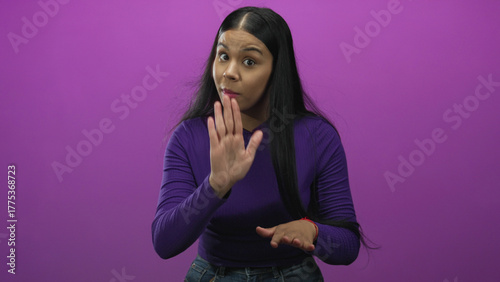 Принти на полотні Young latin woman facing camera slowly gestures with hands out and slightly tilted head in purple studio; caution