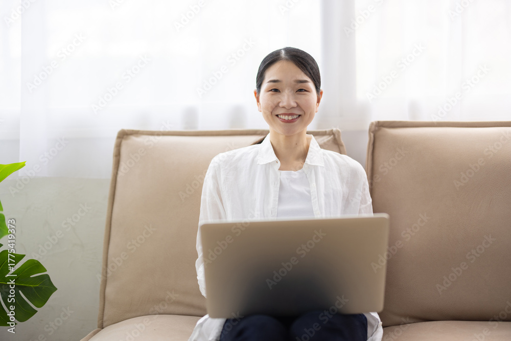 Fototapeta premium Woman Sitting on Sofa Using Laptop in Bright Living Room