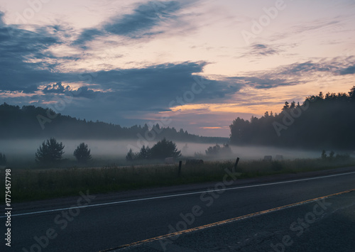 Early morning fog rolls across a field in rural near a two lane road