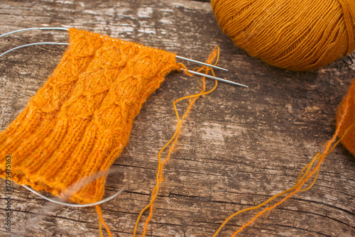Cozy knitted socks with yarn ball and knitting needles. Orange wool socks on wooden background. Cozy autumn colours. Knitting pattern close up. Knitting hobby. Knitwear concept. Needlework background.