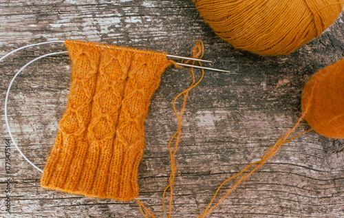 Cozy knitted socks with yarn ball and knitting needles. Orange wool socks on wooden background. Cozy autumn colours. Knitting pattern close up. Knitting hobby. Knitwear concept. Needlework background.