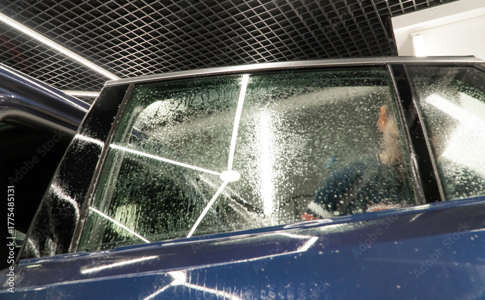 Obraz premium Male car service worker glue window tinting in luxury car detailing car repair the concept of love for cars and protection. Applying tinting foil on a car window in the tuning studio close-up. 