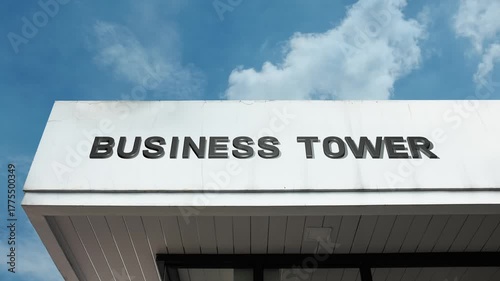 Business Tower word sign prominently displayed on the sleek, glass facade of a towering skyscraper beneath a clear blue sky, signifying a high-rise office building dedicated to major corporate