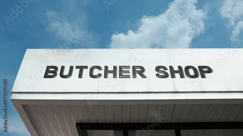Butcher Shop word sign plainly displayed on the commercial facade of a retail building beneath a bright blue sky, signifying a location specializing in cutting, preparing, and selling meat products