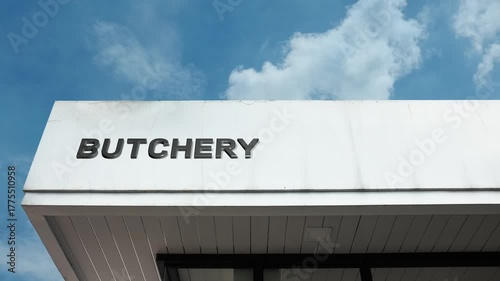 Butchery word sign plainly displayed on the commercial facade of a retail building beneath a bright blue sky, signifying an establishment specializing in the preparation and sale of meat and meat