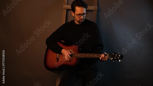 Young male musician playing a guitar melody while standing in a dark studio