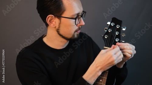 Portrait of a young male musician inserting a string into a guitar

