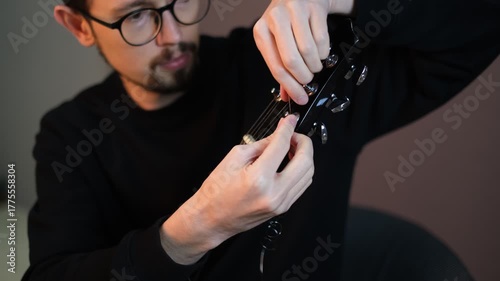 Portrait of a young male musician inserting a string into a guitar


