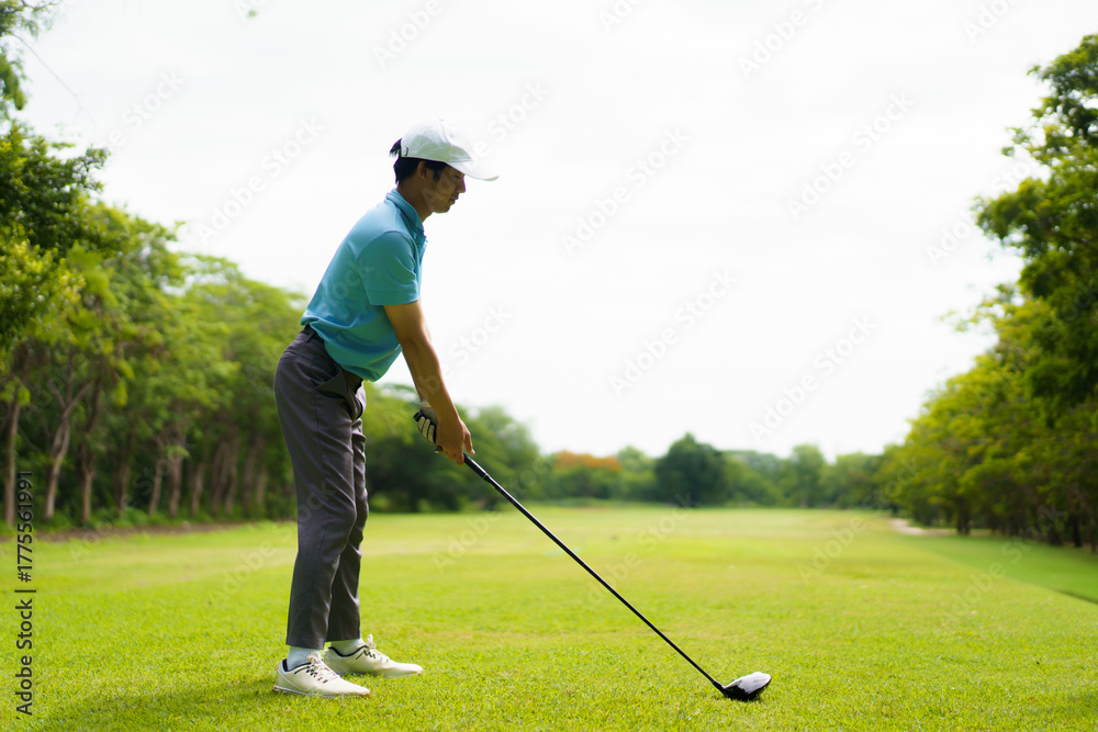 Fototapeta premium Amateur Asian male golfer teeing off in morning sunlight.