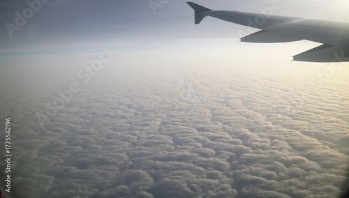 Airplane Window View Above Snowy Clouds, soft pale winter sunlight illuminating white clouds below, peaceful and dreamy aerial travel visuals 