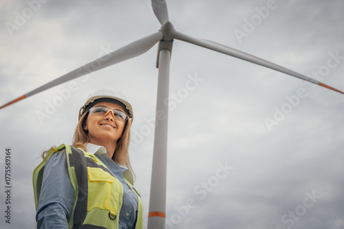 A confident female engineer stands proudly before a towering wind turbine, symbolizing the bright future of renewable energy and our commitment to environmental sustainability for generations