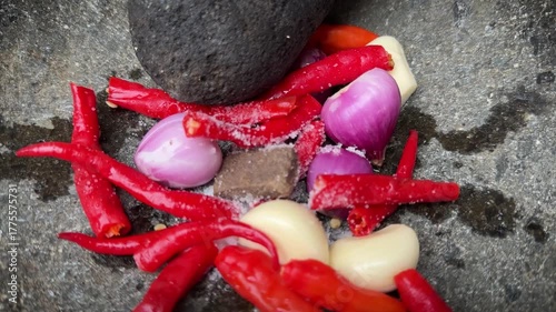 The making of chili paste called sambal , grinding red chili peppers, onion, and garlic in a rough stone mortar and pestle on a cobblestone surface, conveying rustic cooking and fresh spices