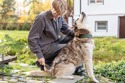 Young caucasian male brushing husky dog in backyard on a sunny day. Mindful childhood, emotional intelligence, responsibility through caring for pets, gentle interaction between child and animal