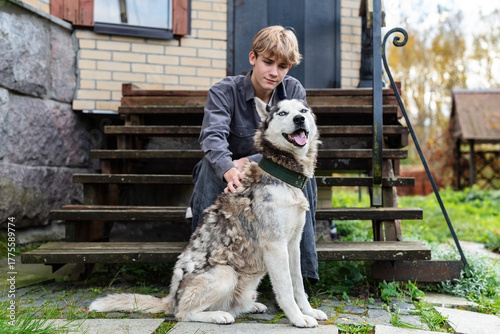 Young caucasian male with husky sitting on wooden steps outside a brick house