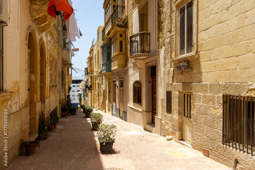 Fototapeta premium An alley between limestone buildings with pots on the middle in Birgu, Malta