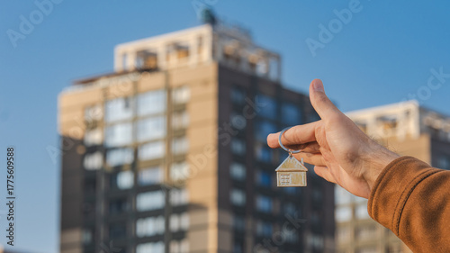 Hand Holding House Keychain on Background of Apartment Building