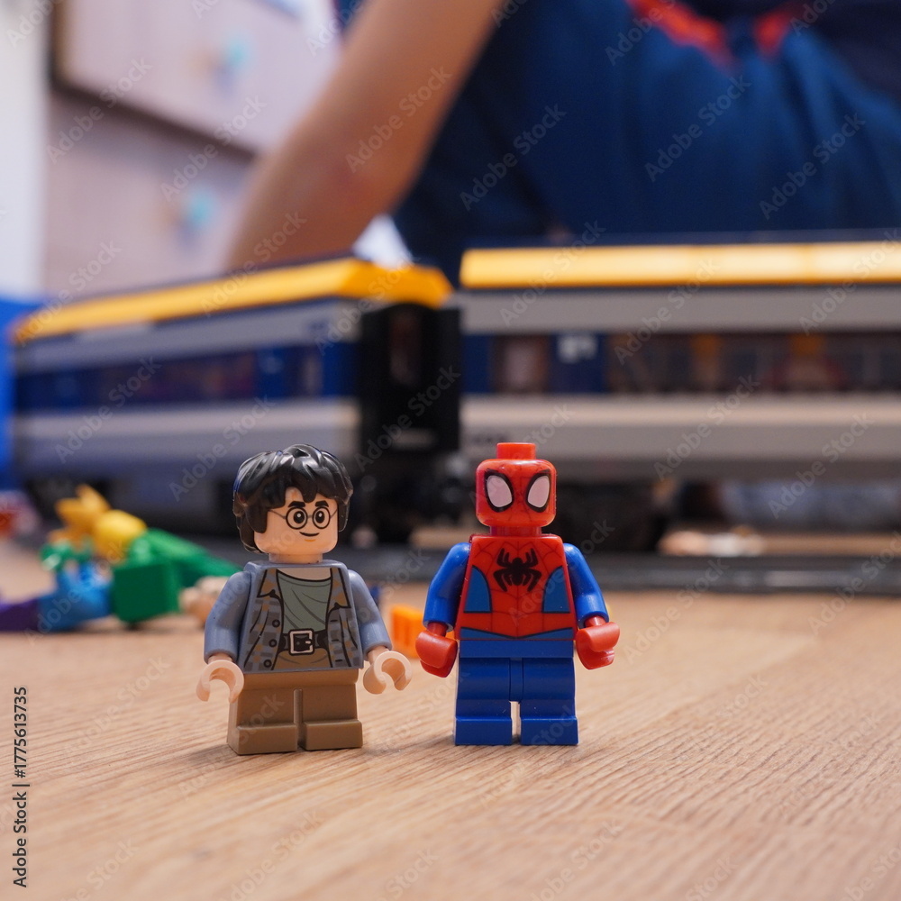 Naklejka premium Lego Spider-Man and Harry Potter figures standing in front of a toy train, showcasing popular culture icons