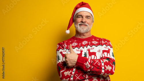 Merry mature man wear knitted christmas sweater Santa hat presenting something on yellow background