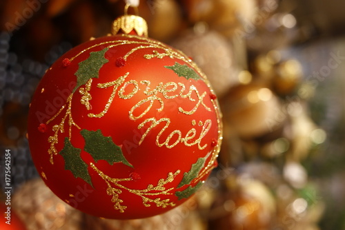 Boule de noël de couleur rouge et or ronde portant l'inscription joyeux noël et des incrustations de feuilles vertes