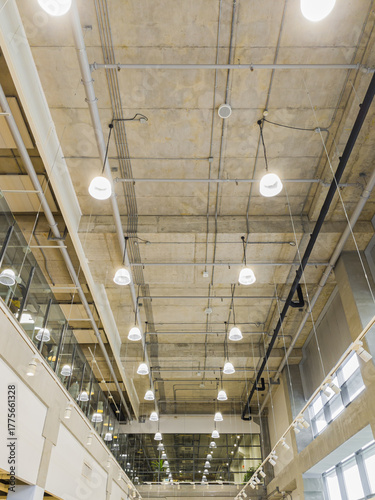 perspective view of exposed air ducts and electrical systems on bare concrete ceiling in modern building.