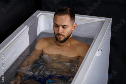 Young man taking an ice bath among ice cubes. Сryotherapy and recovery. Selective focus.