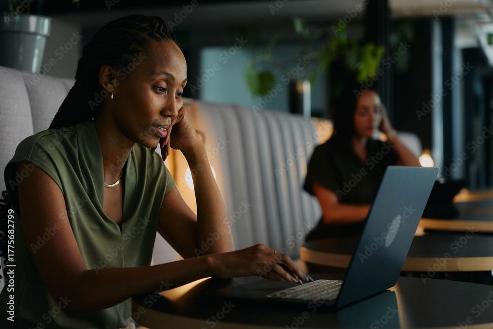Fototapeta premium Tired young black businesswoman using laptop completing work in office lobby