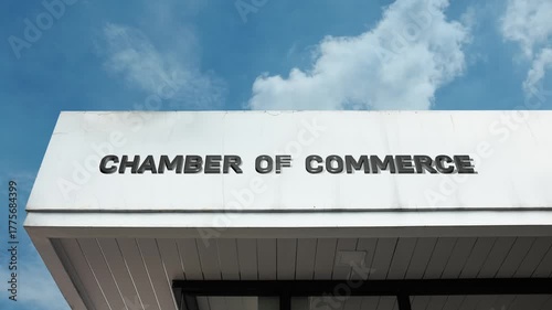 Chamber of Commerce word sign clearly displayed on the official, civic facade of a building beneath a clear blue sky, signifying an association promoting and protecting the interests of local business