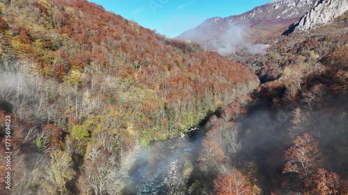 Aerial drone footage of the beautiful Piva River in Montenegro on a dramatic foggy morning, with mist drifting over the mountains and calm turquoise water below.
