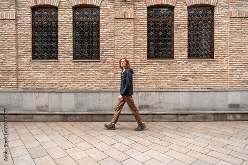 Obraz na plátně Woman walking calmly along brick wall in urban setting during daytime