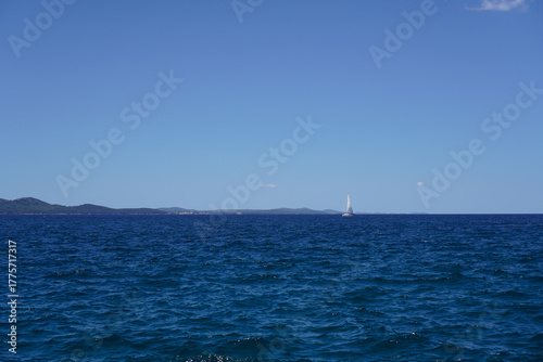 Fotografie White boat far off on vivid blue sea under a bright sunny sky — minimalistic mar