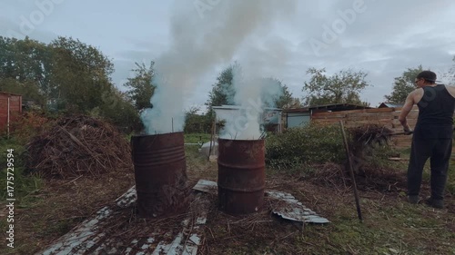 A man burns grass in an iron barrel, burning grass in a barrel, burning grass in a cottage