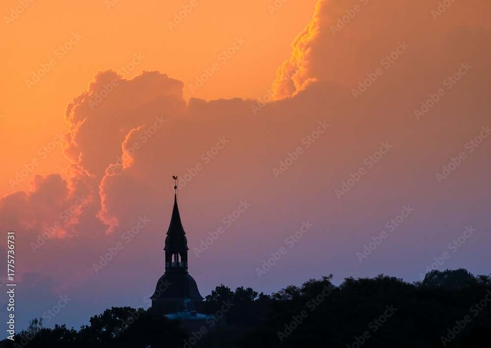 Obraz premium Silhouette of historic steeple against vibrant sunset sky with dramatic cloud formations