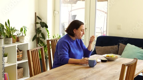 Woman is eating launch at the table at the kitchen