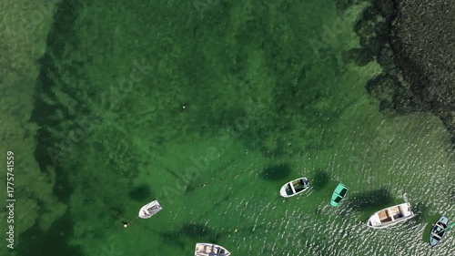 Aerial view of a calm, emerald green sea filled with small boats