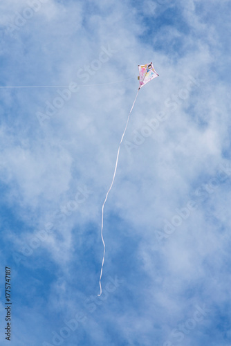 Kite flying high up in blue sky with long white streamer trailling from it