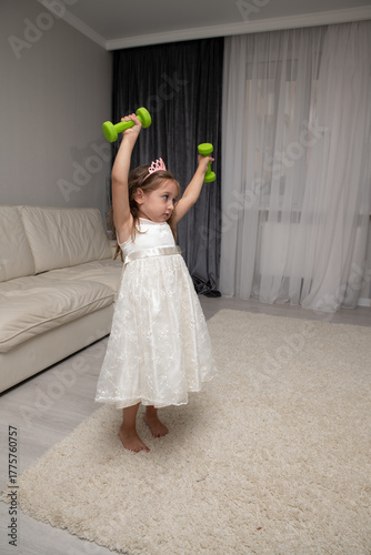 Wallpaper Mural A little girl in a princess dress exercises with dumbbells on TV. Selective focus, real photo. Torontodigital.ca
