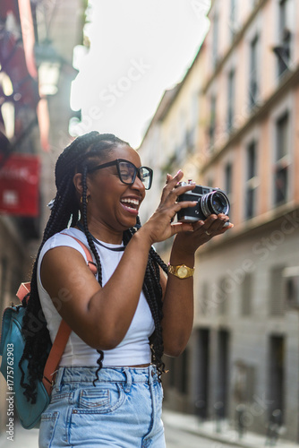Smiling Latina woman with braided hair using an analog camera on the street