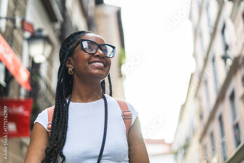 Smiling Latina woman with braided hair using an analog camera on the street